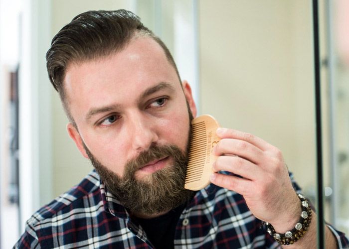Man spreading beard oil with a comb 